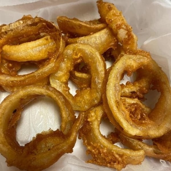 Golden-brown, crispy onion rings from Olympus Diner, served in a white paper container.