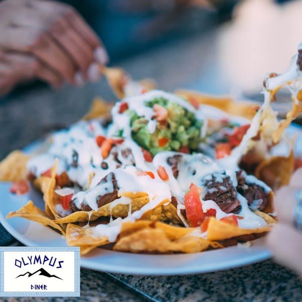 A plate of Olympus Diner nachos with beef, cheese, guacamole, sour cream, and tomatoes.