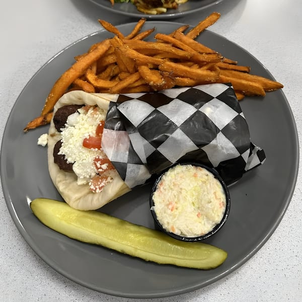 Olympus Diner gyro with sweet potato fries, coleslaw, and a pickle spear on a gray plate.