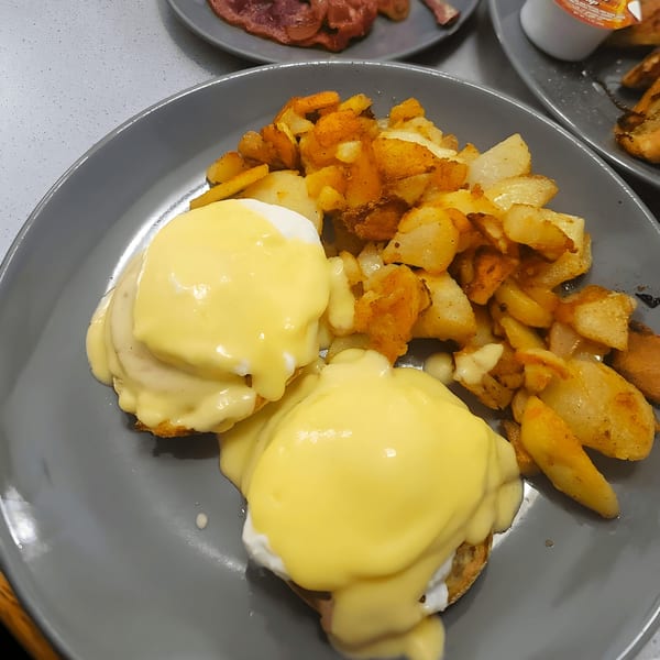 Eggs Benedict with hollandaise sauce and a side of home fries on a gray plate at Olympus Diner.
