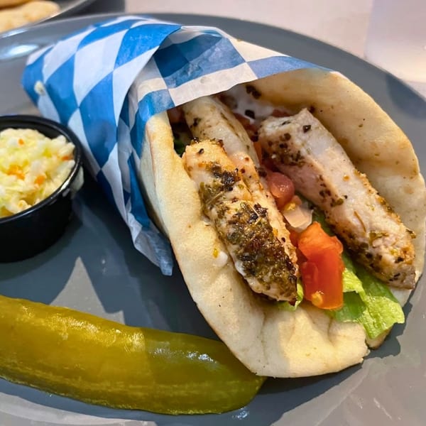 Grilled chicken gyro with lettuce, tomato, coleslaw, and a pickle spear on a gray plate.