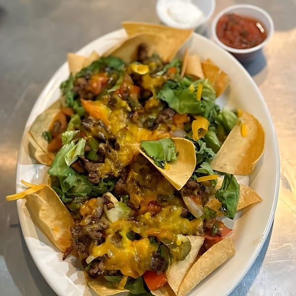 Olympus Diner's nachos with melted cheese, ground beef, lettuce, and salsa on a white plate.