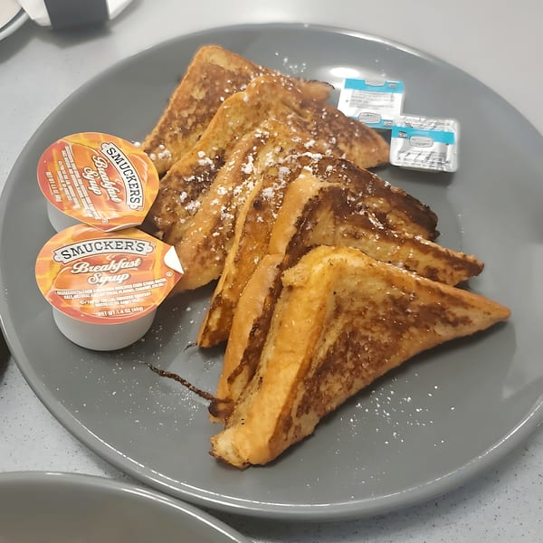 French toast triangles dusted with powdered sugar, served with Smucker's syrup and butter on a gray plate.