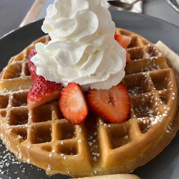 Golden waffle topped with whipped cream, fresh strawberries, and powdered sugar on a gray plate.