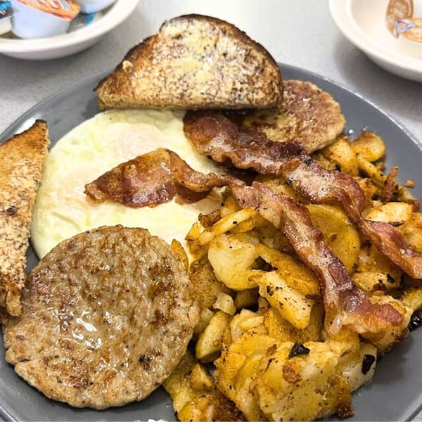 A diner breakfast plate with eggs, bacon, sausage, home fries, and buttered toast.