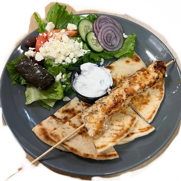 A Greek platter with chicken souvlaki, pita bread, tzatziki, dolmades, and a Greek salad.